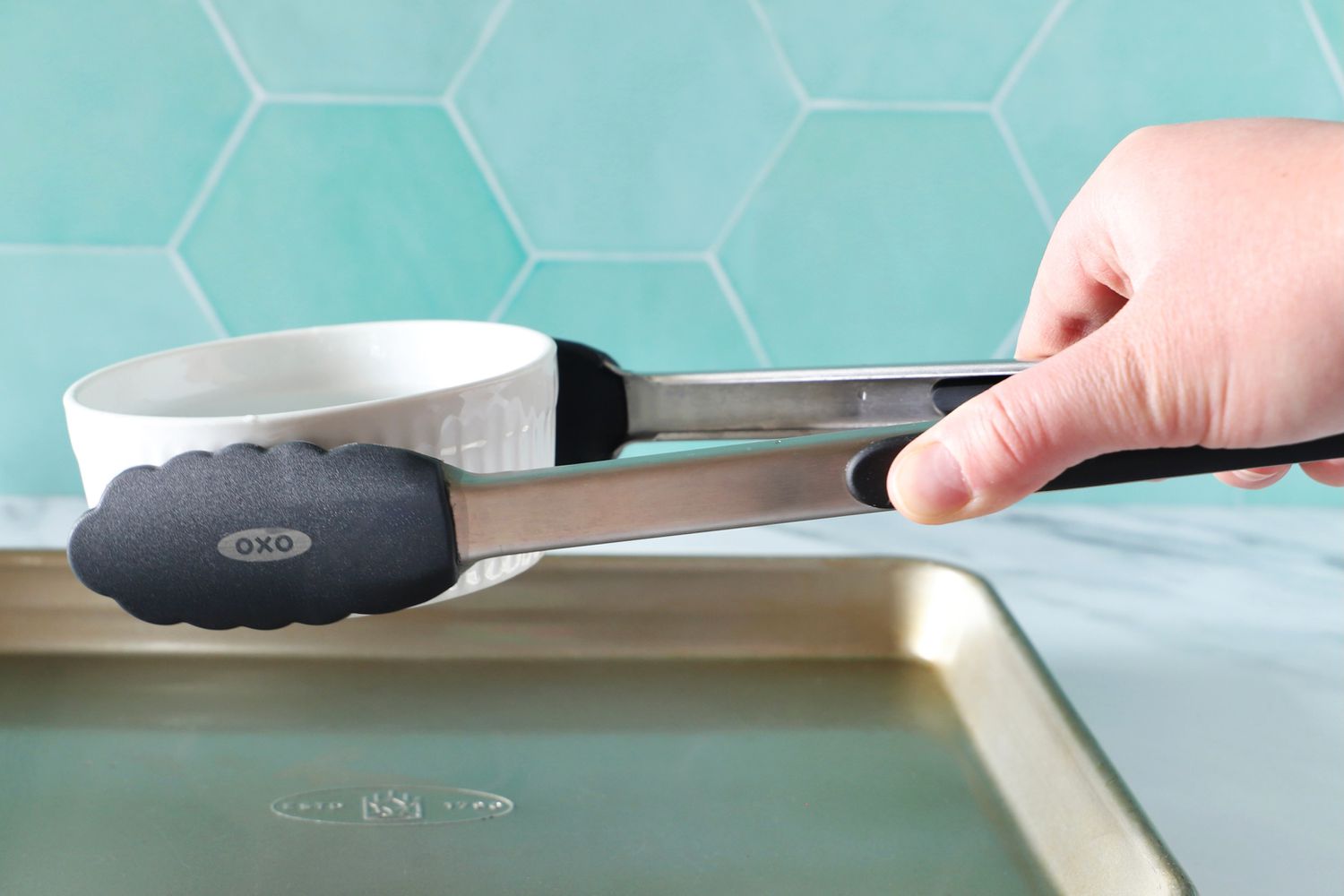 Hand using the OXO 12-Inch Silicone Tongs to pick up a souffle dish