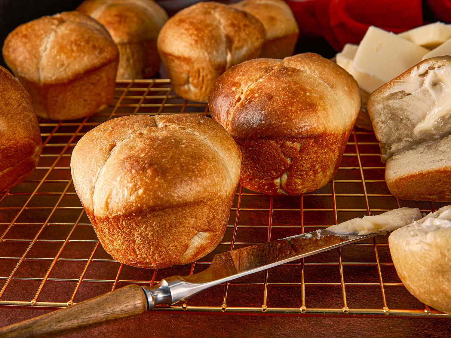 Freshly baked cloverleaf rolls on a wire rack with a butter knife and slices of butter