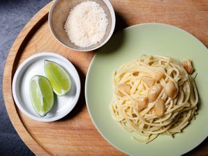 Overhead view of a plate of garlic pasta with grated cheese and lime wedges alongside