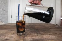 A person pouring cold brew from the Ovalware's carafe into a glass with ice.