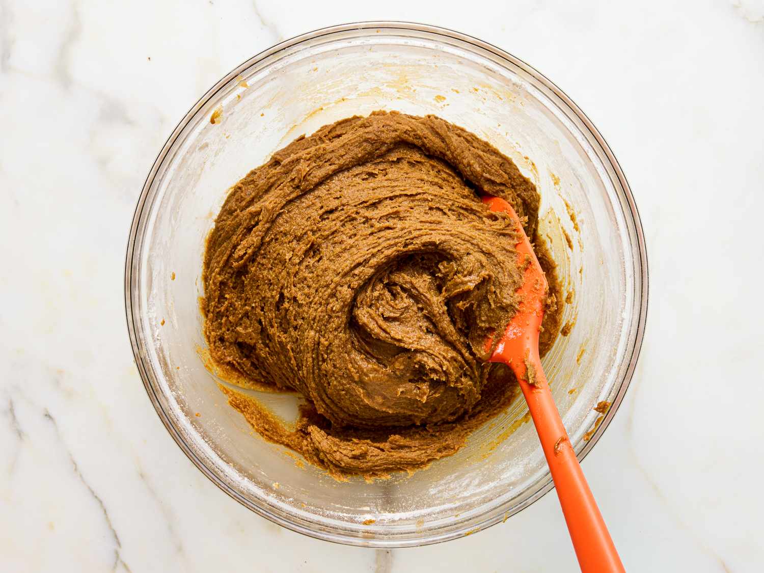 A bowl of gingerbread cookie dough with a red spatula
