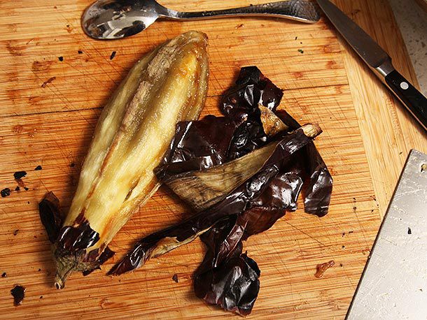 Peeled eggplant next to discarded eggplant skin on a wooden cutting board