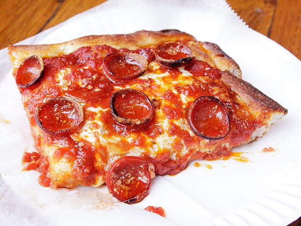 A slice of Prince Street pepperoni pizza on a tissue and white paper plate; the pepperoni edges are curled and slightly browned.