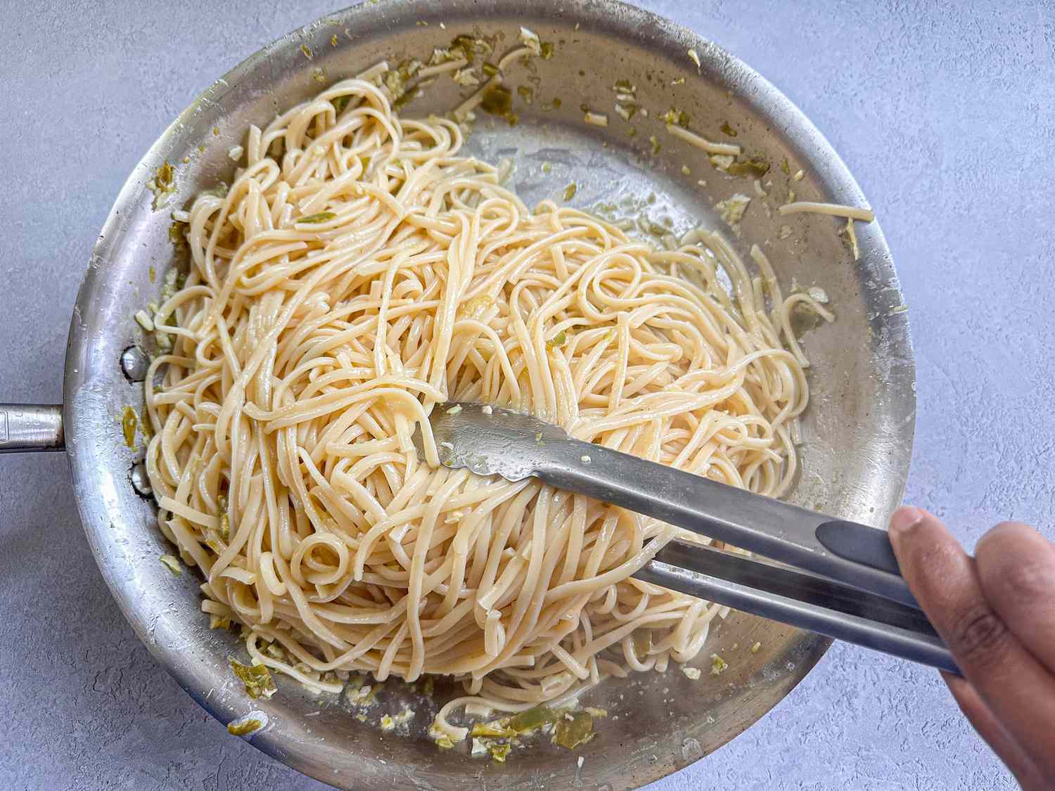 Cooked spaghetti being stirred in a skillet with a pair of metal tongs