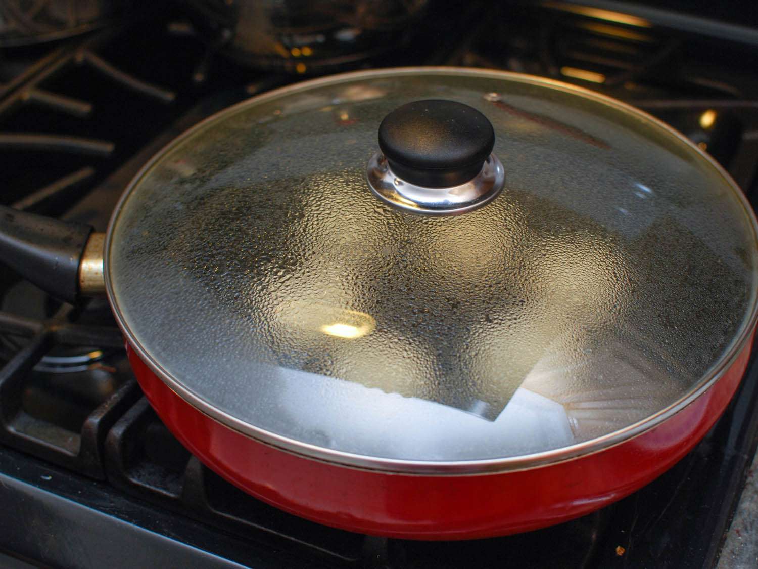 The skillet full of sheng jian bao is covered so that they steam and cook through.