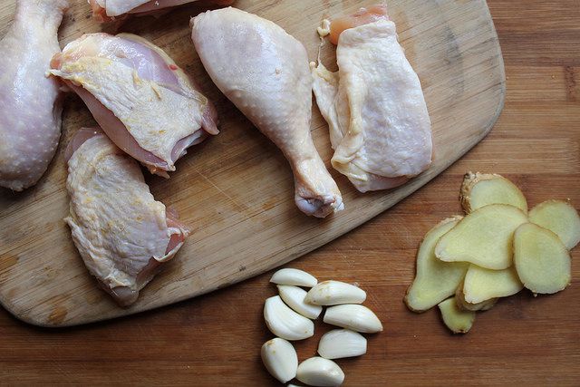 Cutting board with pieces of raw chicken, garlic cloves, and sliced ginger