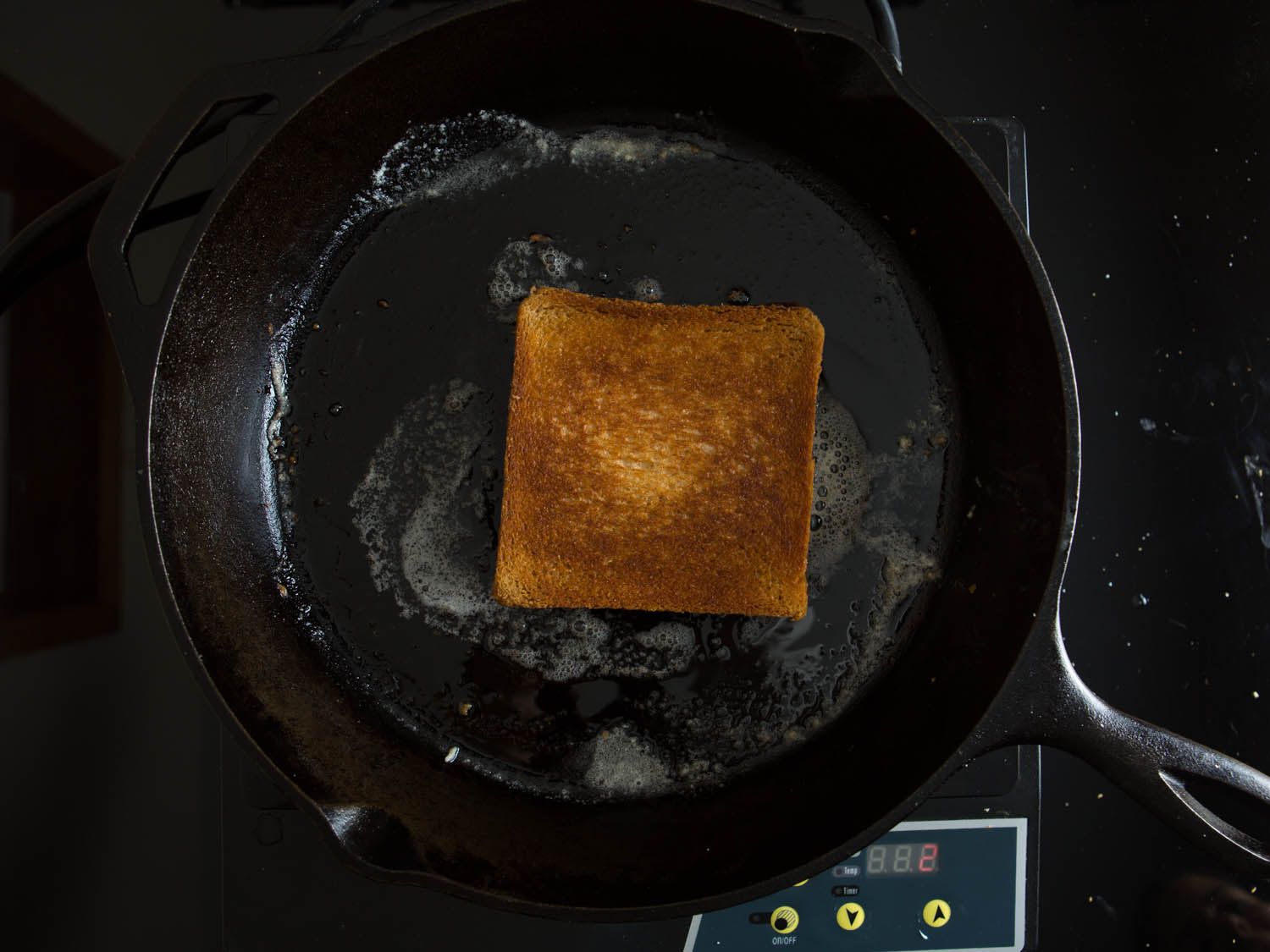 A golden brown grilled cheese sandwich in the middle of a buttered cast iron skillet on a hot plate.