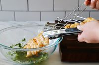 A person pulling shrimp off of two metal skewers using tongs