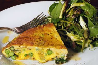 A slice of asparagus-sweet pea frittata, served on a plate with a minty spring salad.