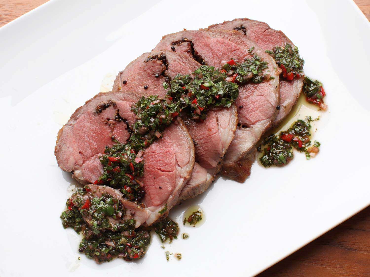 Shingled slices of medium rare lamb leg with chimichurri sauce down the middle