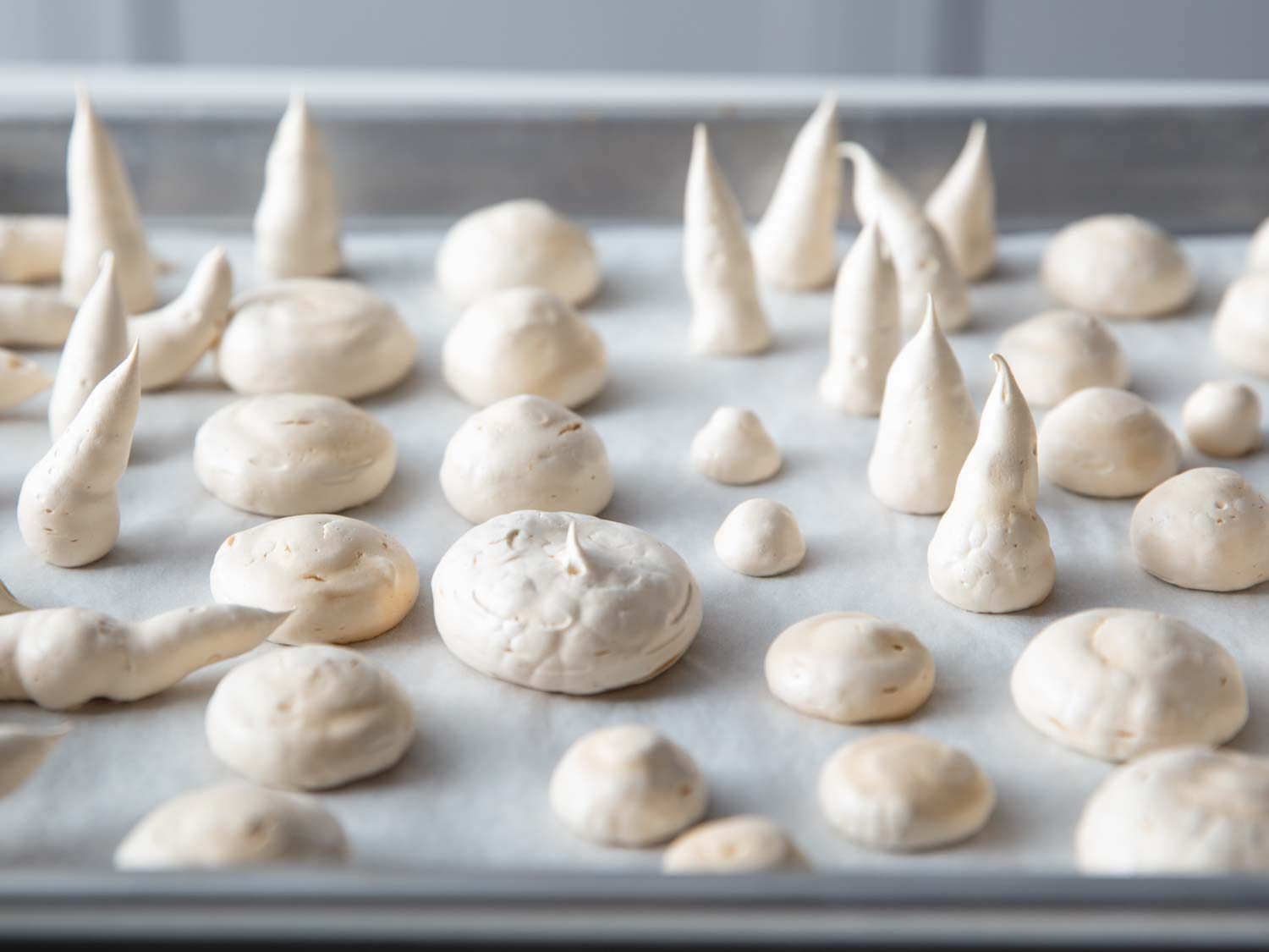 A tray of baked meringue mushroom caps and stems, with a dry, matte ivory finish