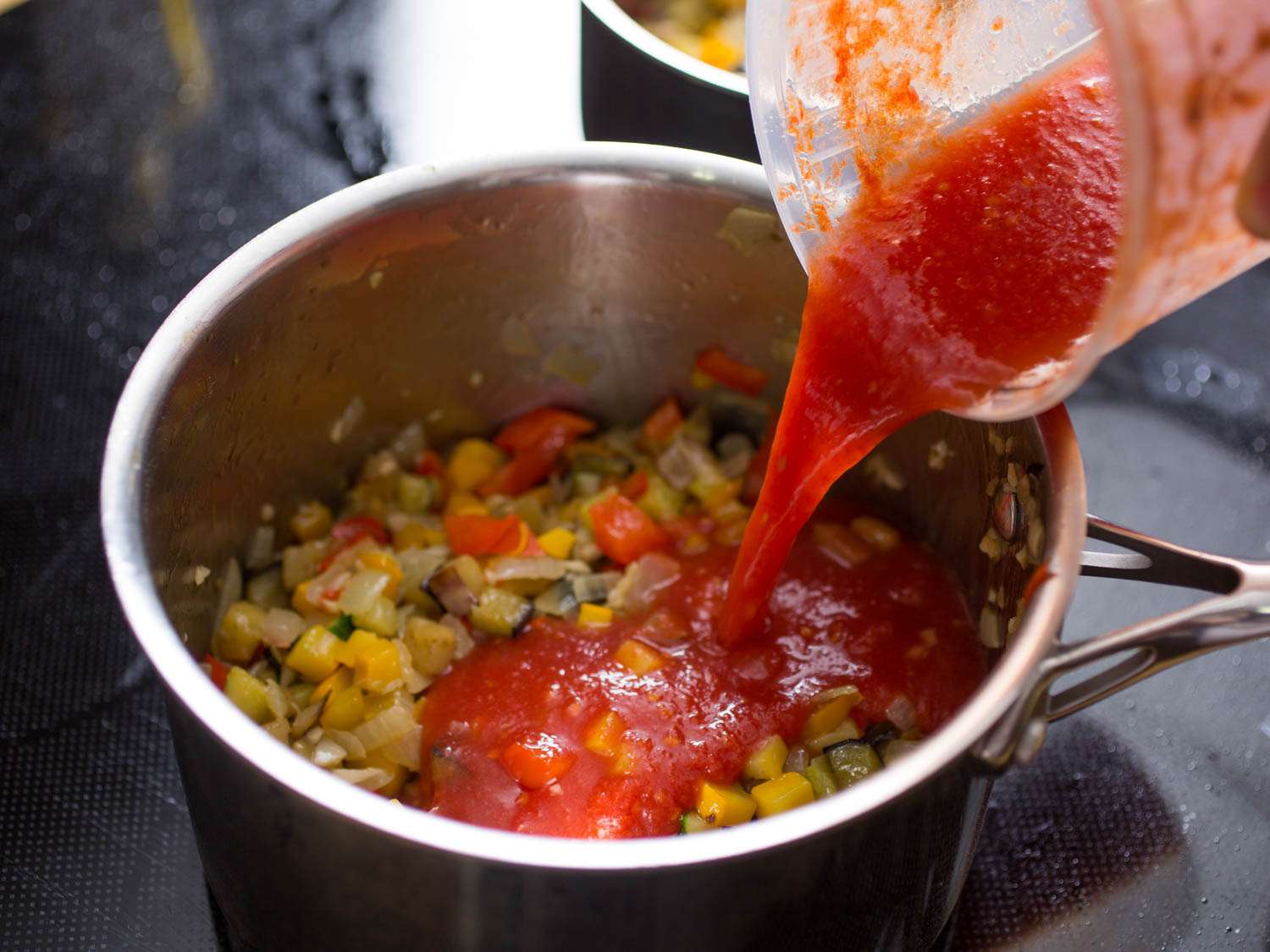 Author pouring tomato purée into saucepan of ratatouille.