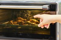 A hand pointing to chicken cooking in the KitchenAid Dual Convection Countertop Oven with Air Fryer