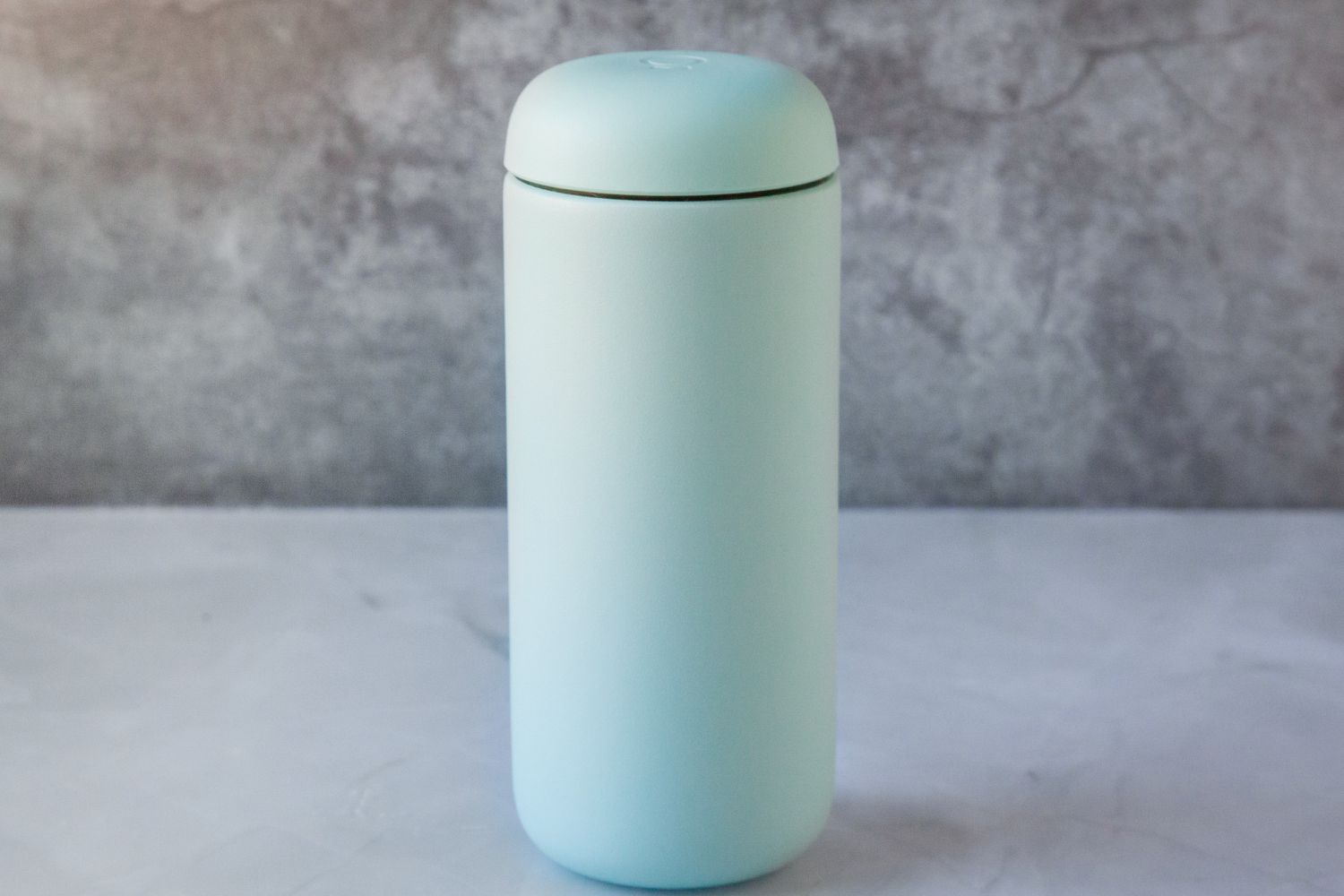 A blue travel mug on a marble countertop.