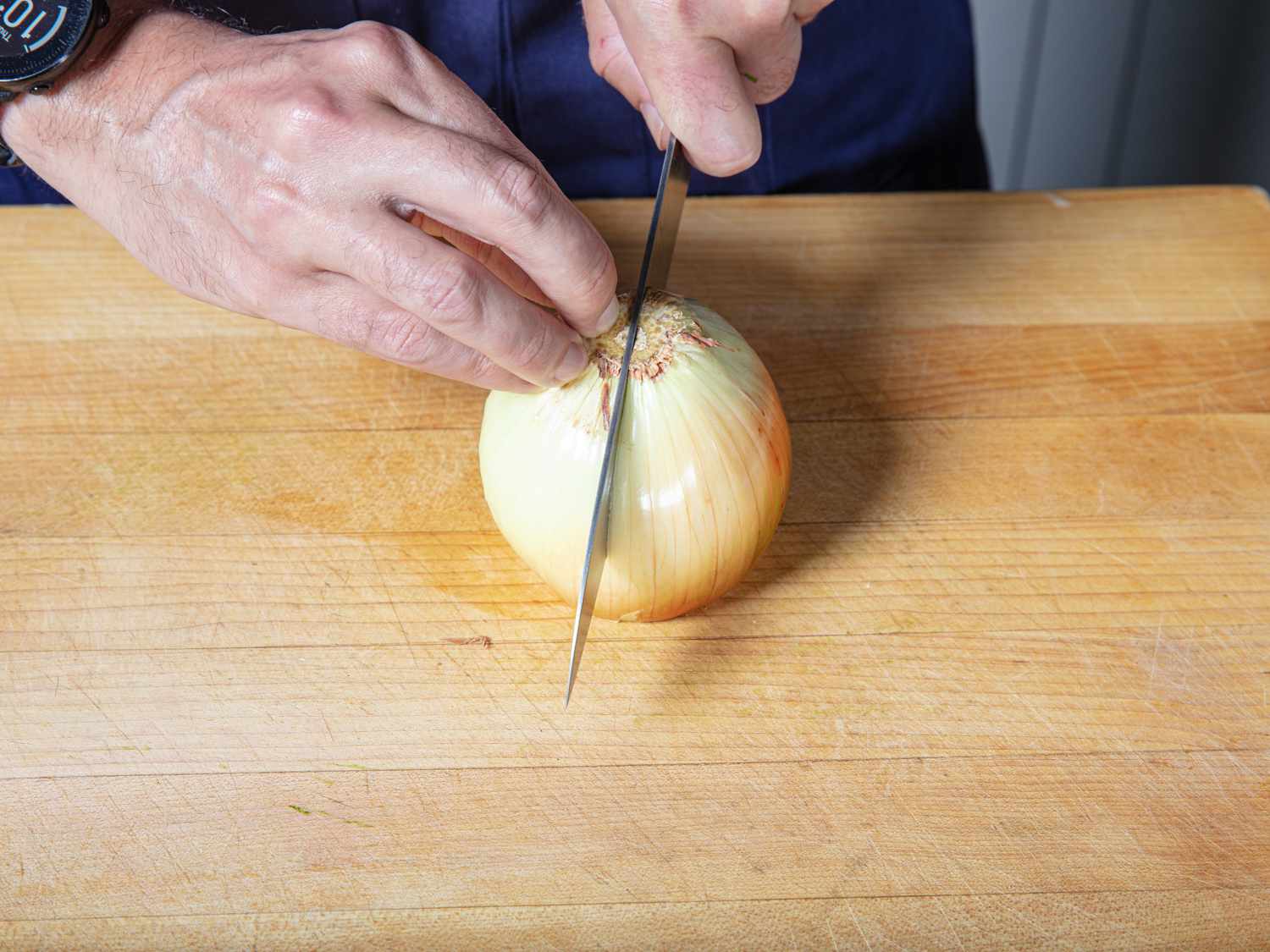 Slicing a peeled onion in half on a cutting board.
