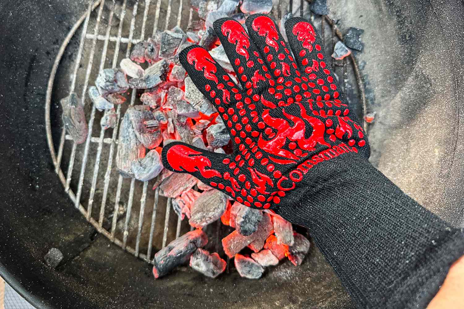 A person hold their hand to hot coals while wearing the Comsmart BBQ Gloves