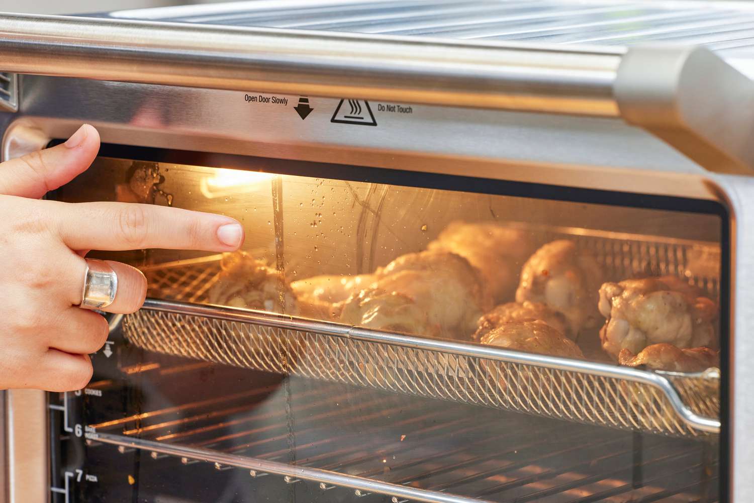 A finger pointing to chicken cooking in the Breville the Smart Oven Air Fryer