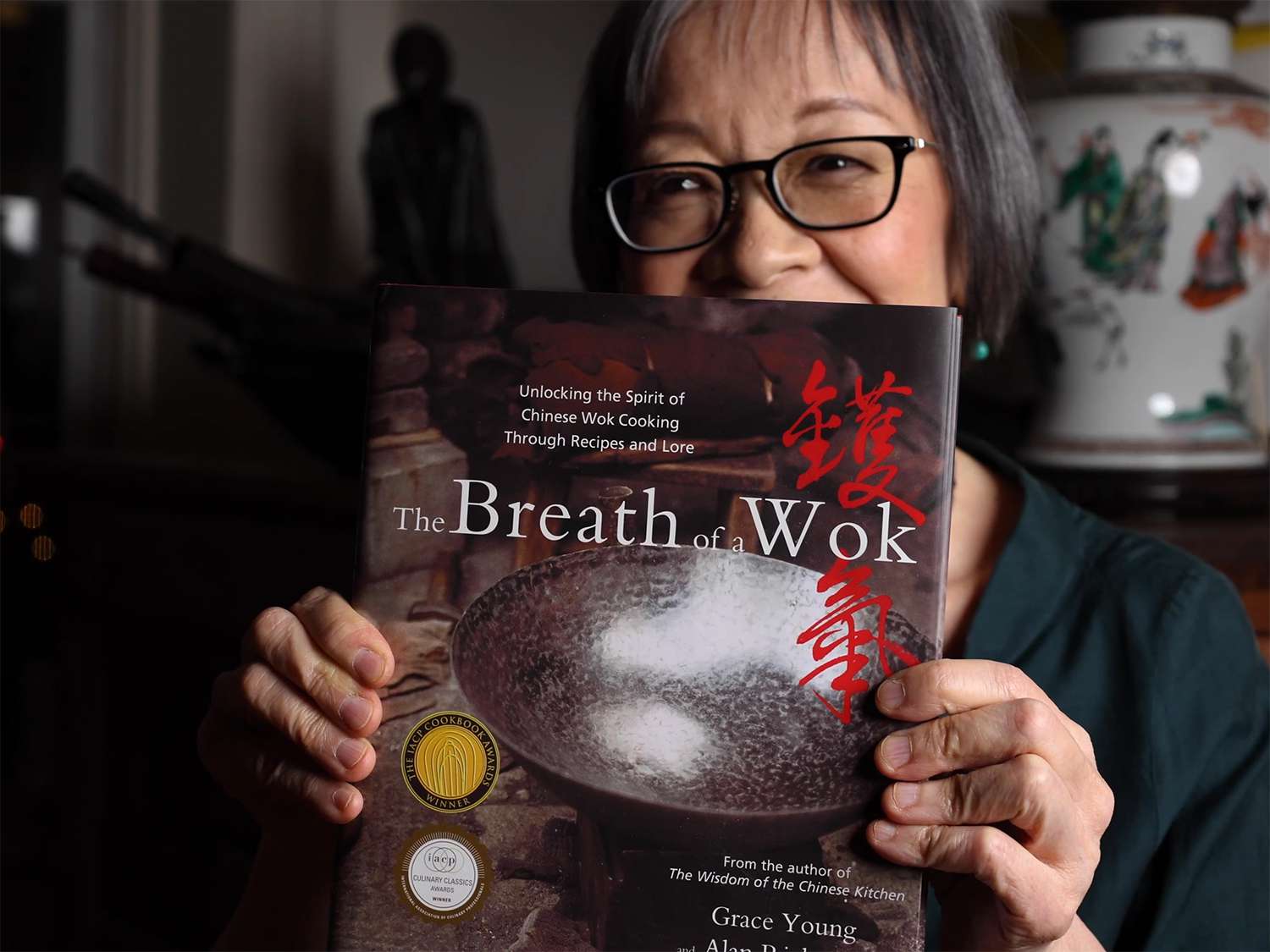 Grace Young holding her book, the Breath of the Wok, in front of her face to the camera