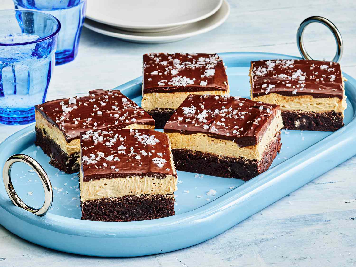 Buckeye Brownies with sea salt garnish, cut into pieces on a blue dish, with blue cups and small white plates 