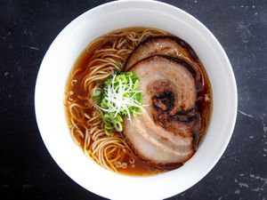 Overhead shot of a bowl of ramen in broth topped with sliced of pressure-cooked pork belly chashu and garnished with sliced scallion. 
