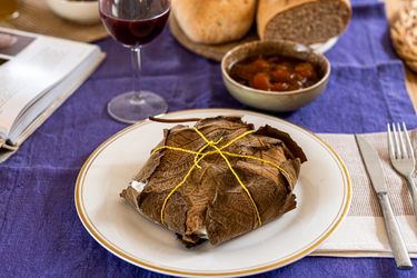 A wrapped dish on a plate bread and bowl of food in the background on a table