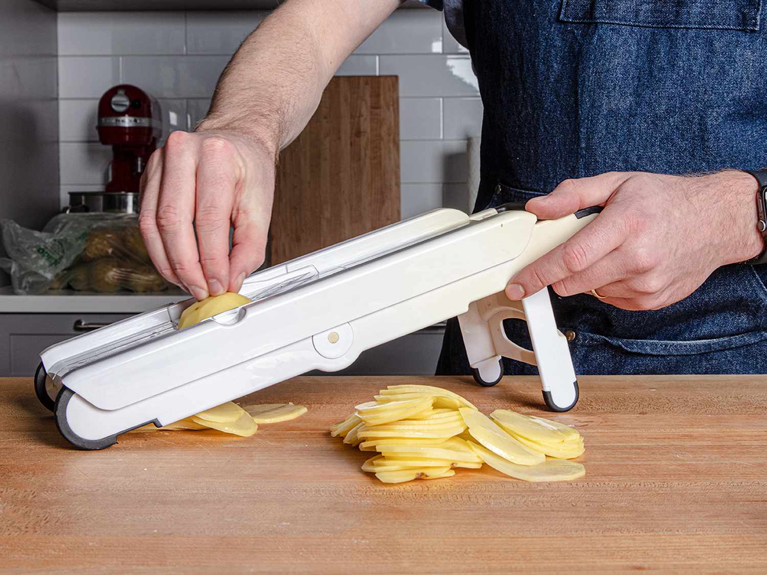 Waxy potatoes being sliced on a white plastic mandoline.