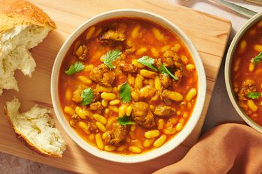 2 bowls of Loubia Stew on a wooden board with bread on the side and fabric napkin on the bottom of photo