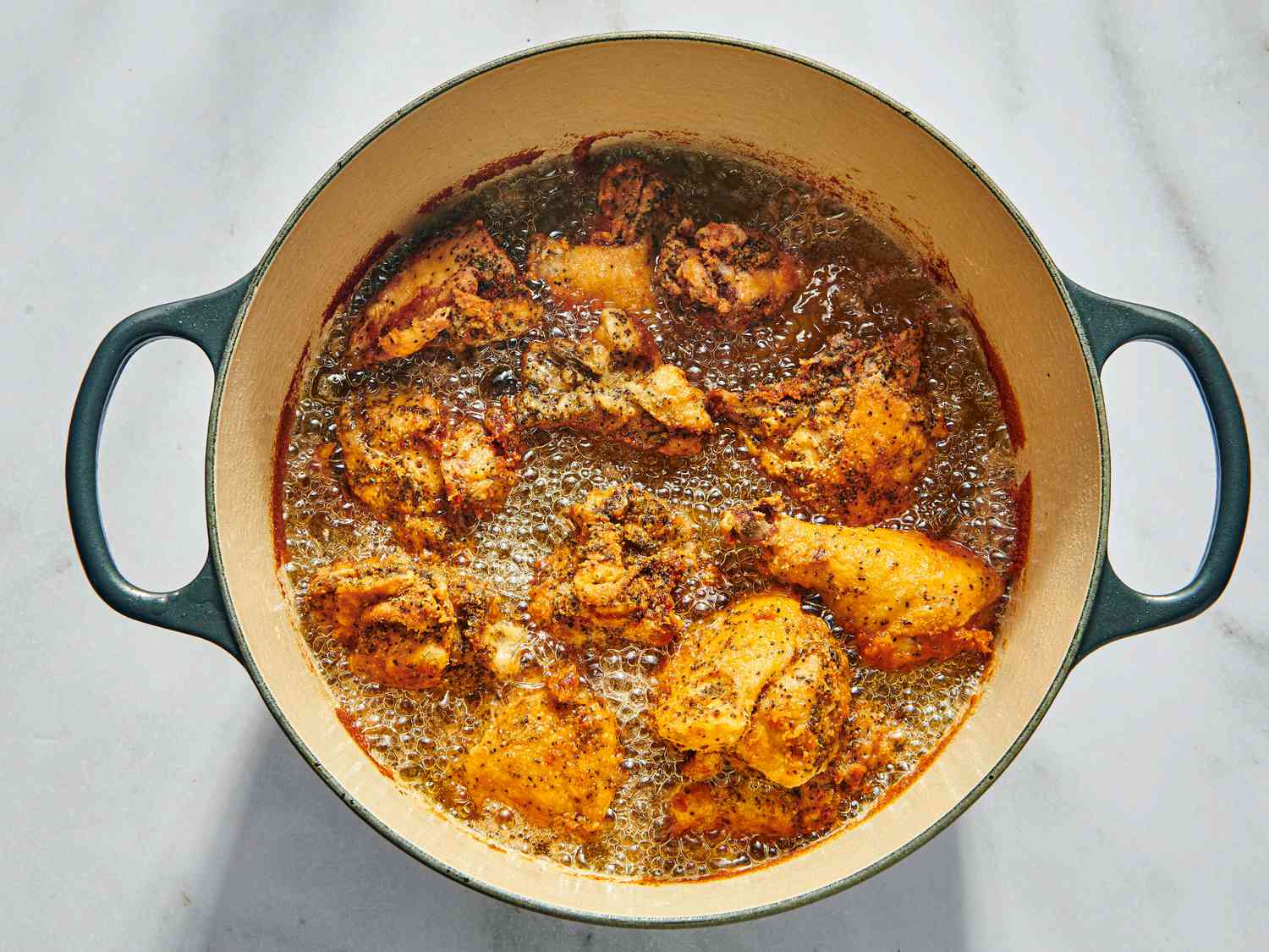 Chicken frying in a dutch oven on white marble 