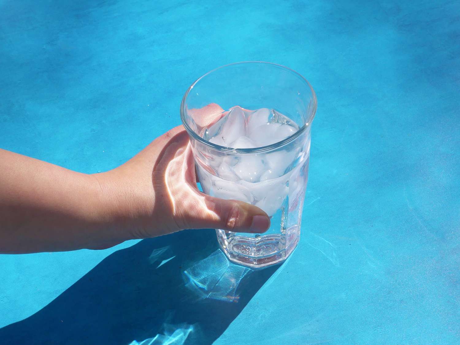 hand holding duralex with ice and seltzer in it over blue backdrop