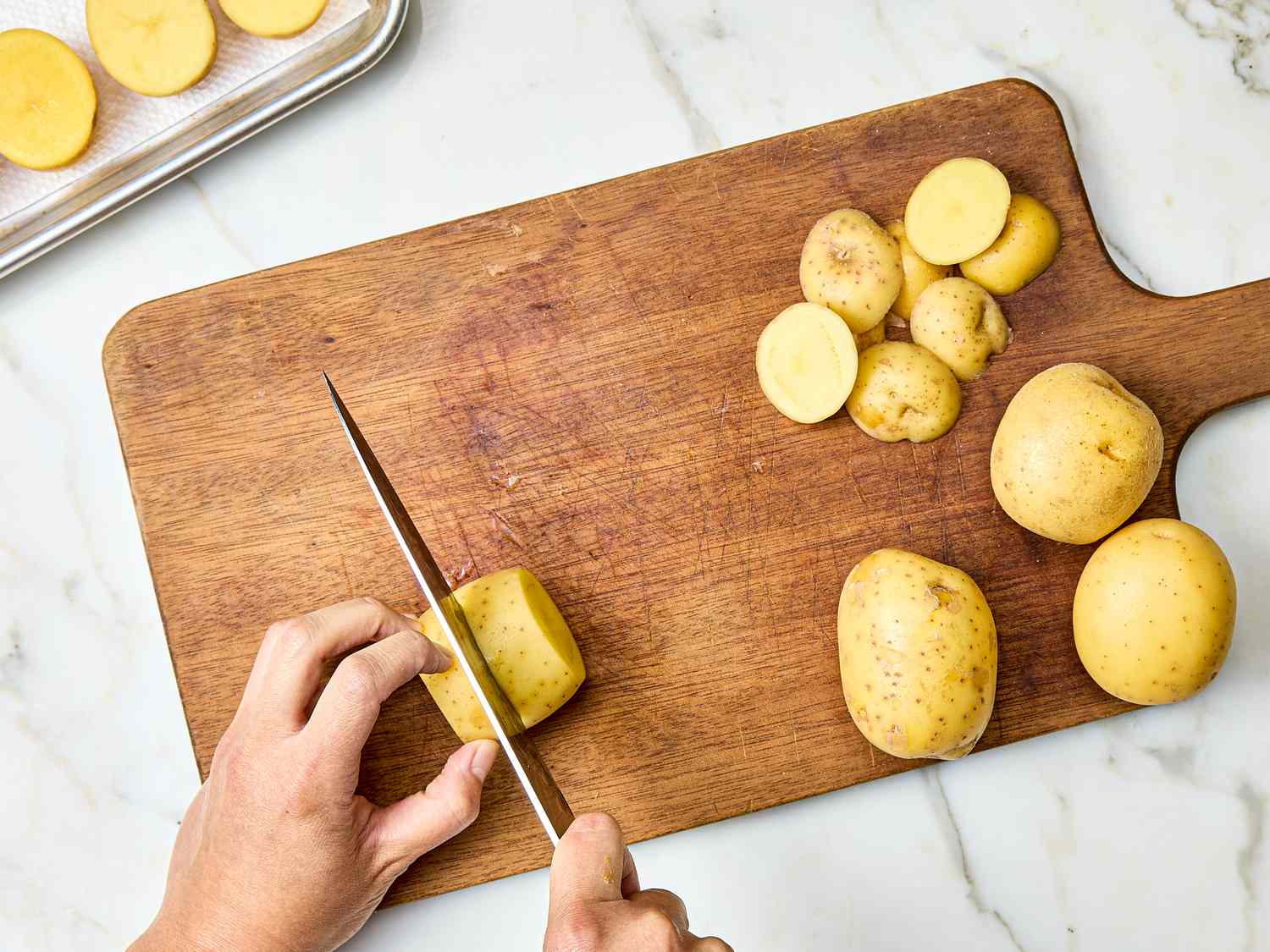 Slicing potatoes on a wooden cutting board with a knife some slices and whole potatoes visible