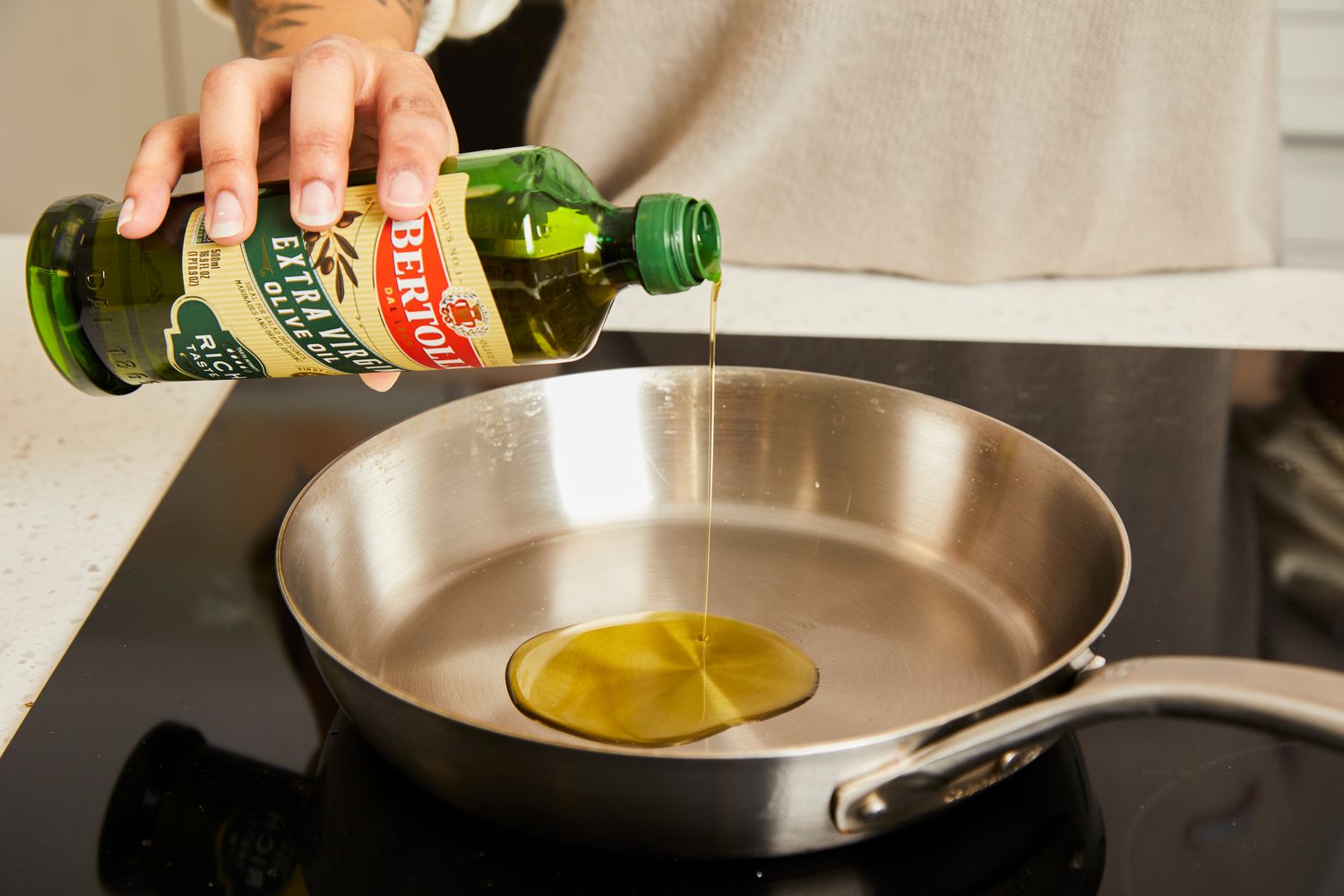 Bertolli olive oil being added to a stainless steel skillet.