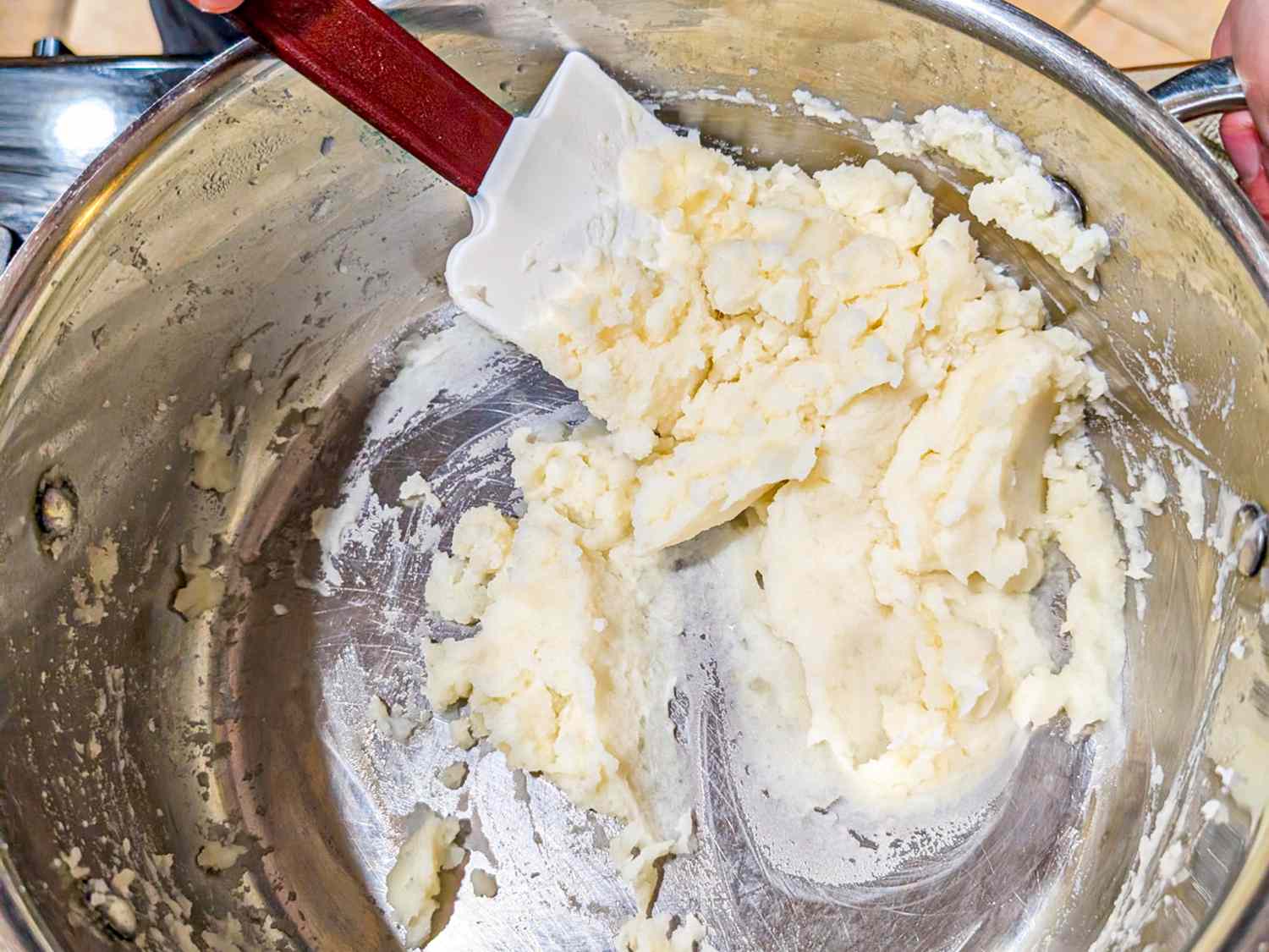 A saucepan with mashed potatoes being mixed using a white spatula
