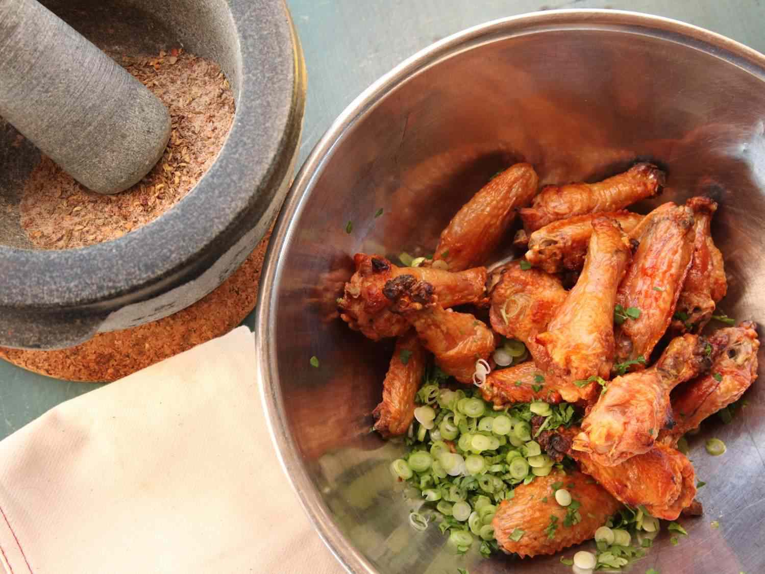 Oven-fried spicy chicken wings being tossed with chopped scallions.