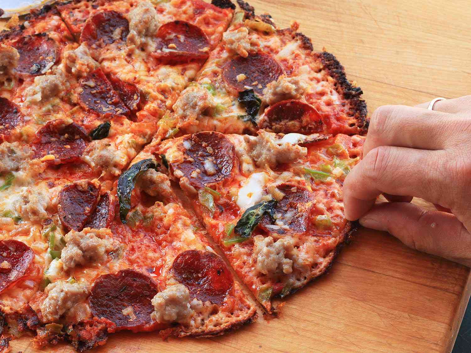 Author picking up a piece of the supreme tortilla pizza.