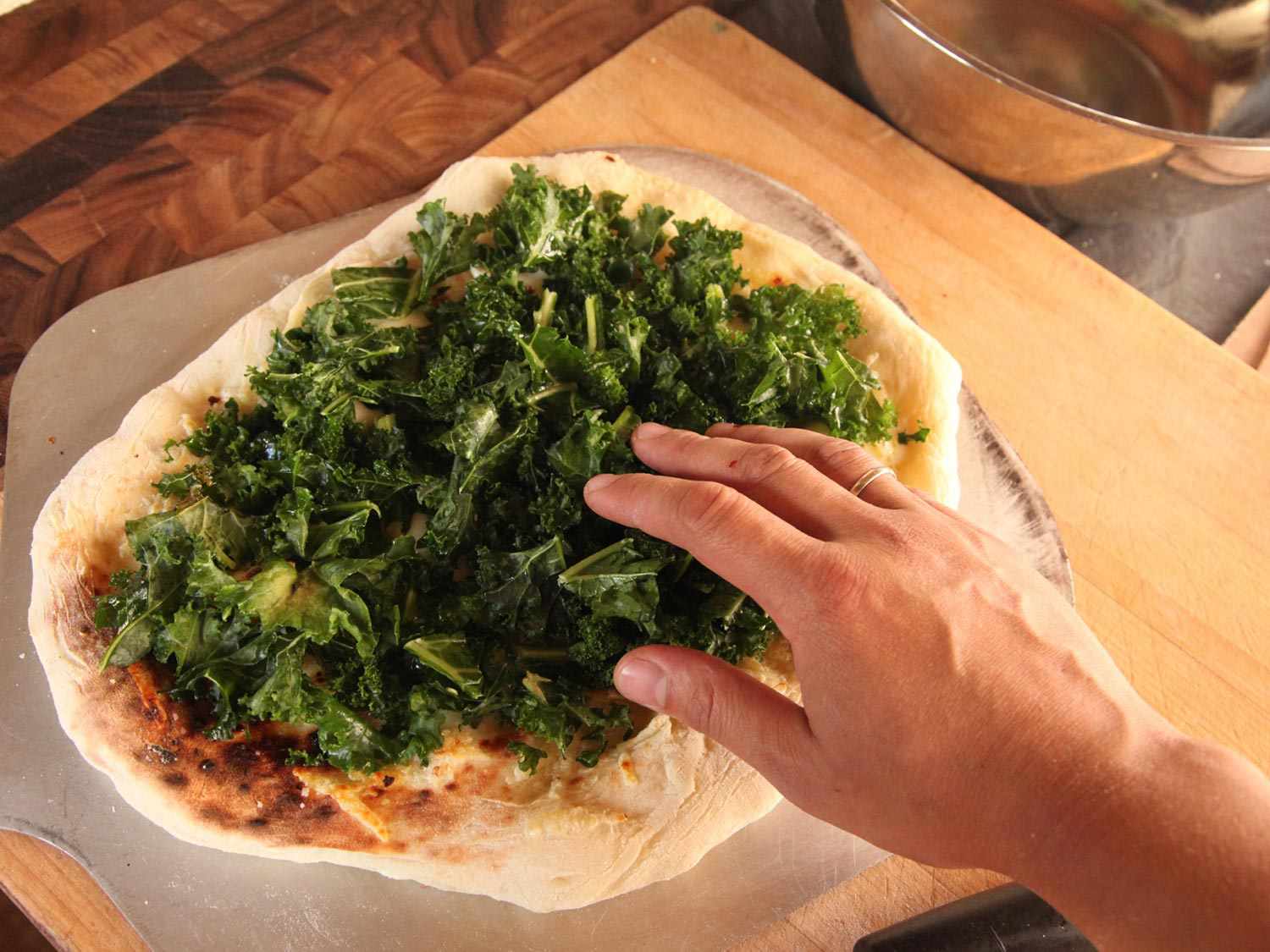 Spreading kale on a partially baked pizza dough. 