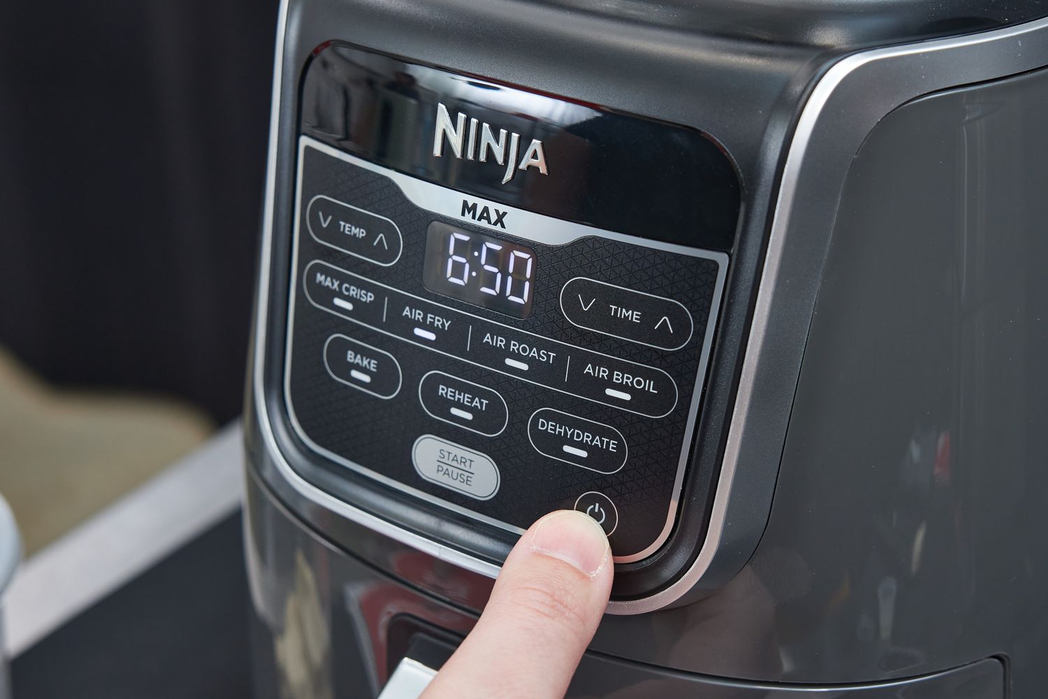 A person pressing the power button on an air fryer's control panel.
