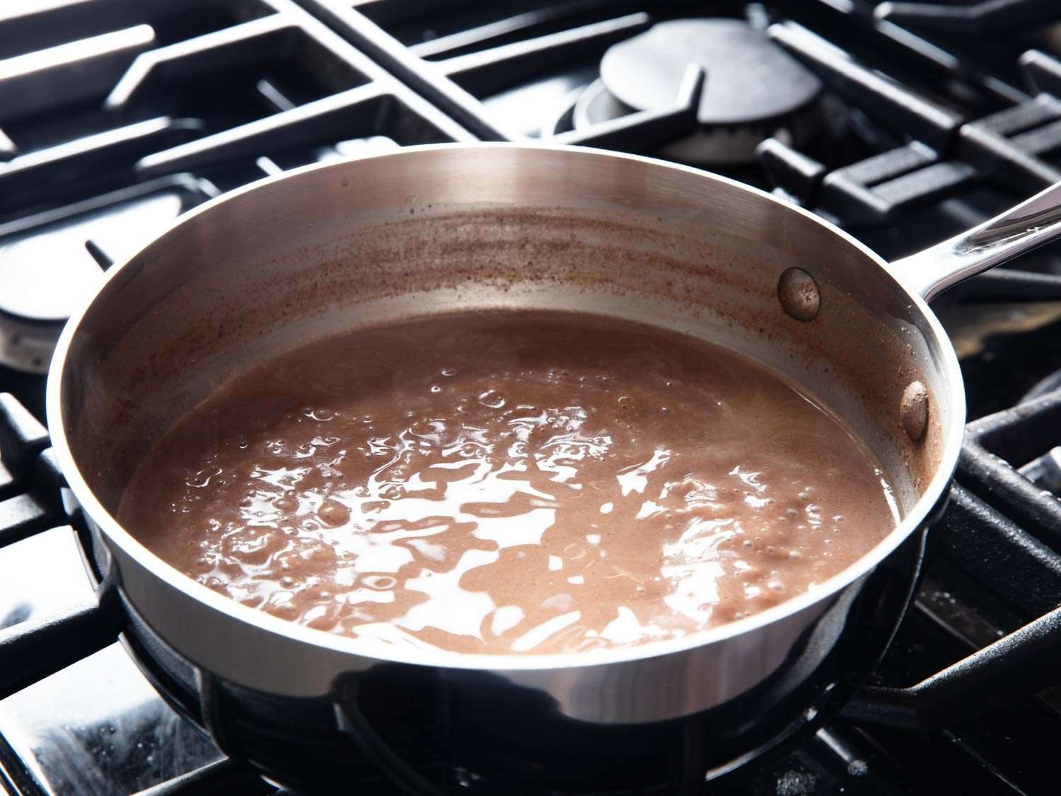 A mixture of pecan-nut puree and water simmers in a saucepan on the stovetop; you can see from residue on the inner walls of the pot that it has already reduced quite a bit.