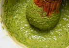 Closeup of a bowl of pesto being mixed with a wooden pestle