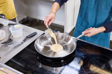 Person pouring batter into a stainless steel fry pan on a stove