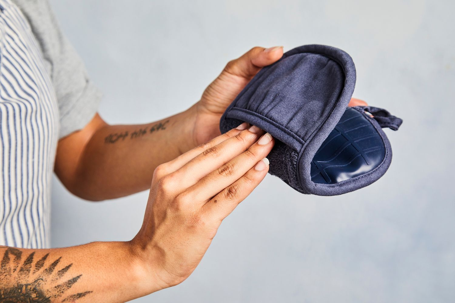 One hand holding a Crate & Barrel pot holder while the other one puts it on.