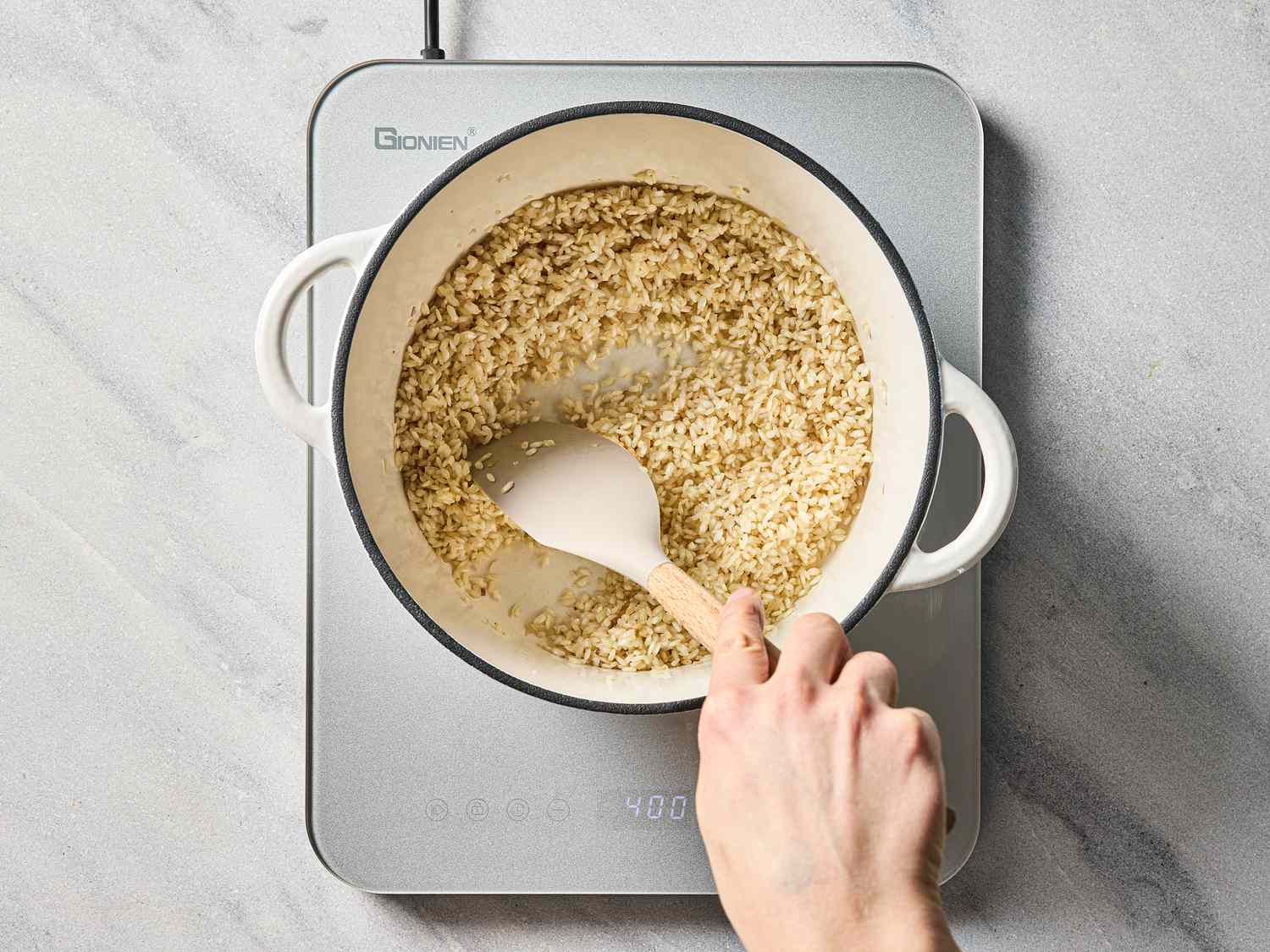 A hand stirring risotto ingredients in a pot on a stove