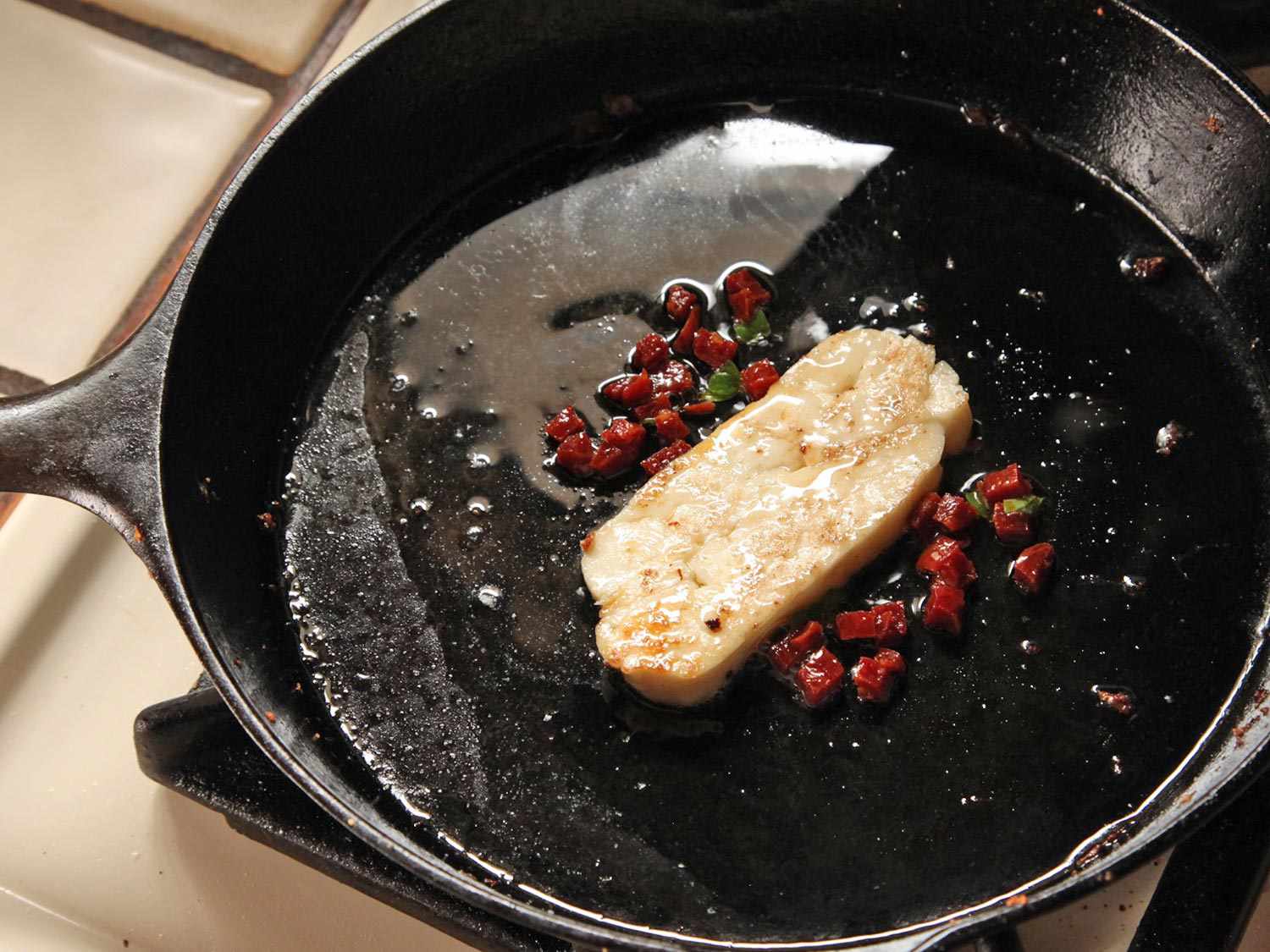 A slice of halloumi and small pieces of chorizo frying in a cast iron skillet