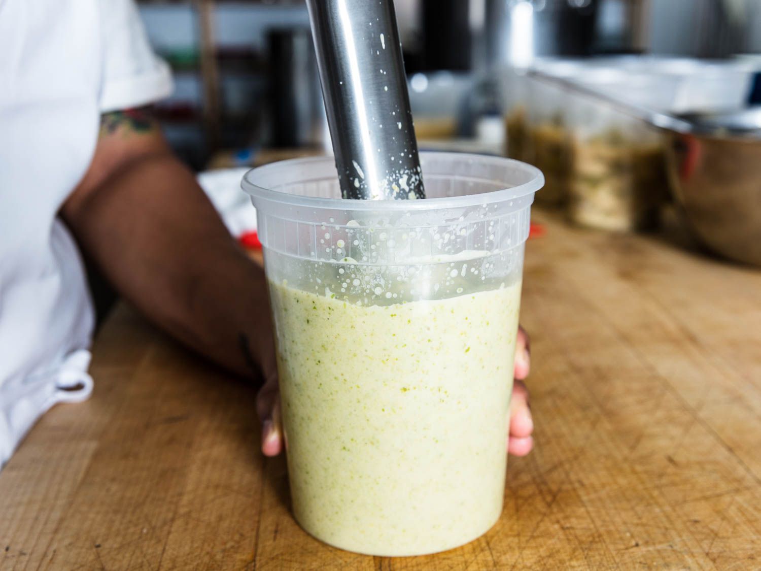 Puréeing celery soup in a plastic container using an immersion blender.