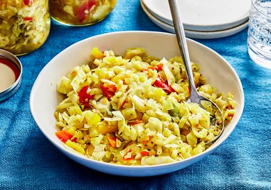 Bowl of Chow Chow with a spoon in it. The bowl is on a blue table cloth with other plates and sparkling water around it 