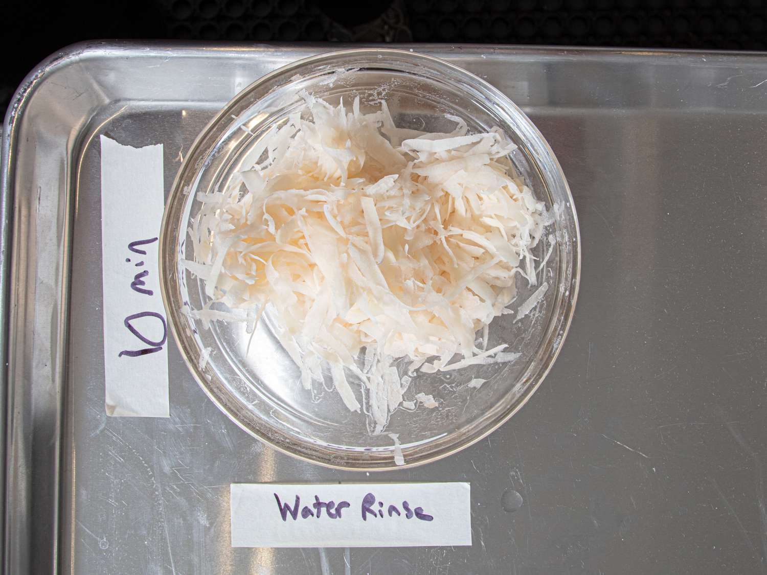 Shredded food sample in a bowl labeled Water Rinse on a metal tray