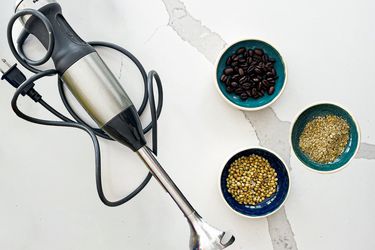 Immersion blender next to three bowls of coffee beans and spices
