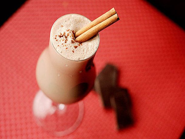 Chocolate and spice eggnog, served in a stemmed glass with a cinnamon stick garnish.