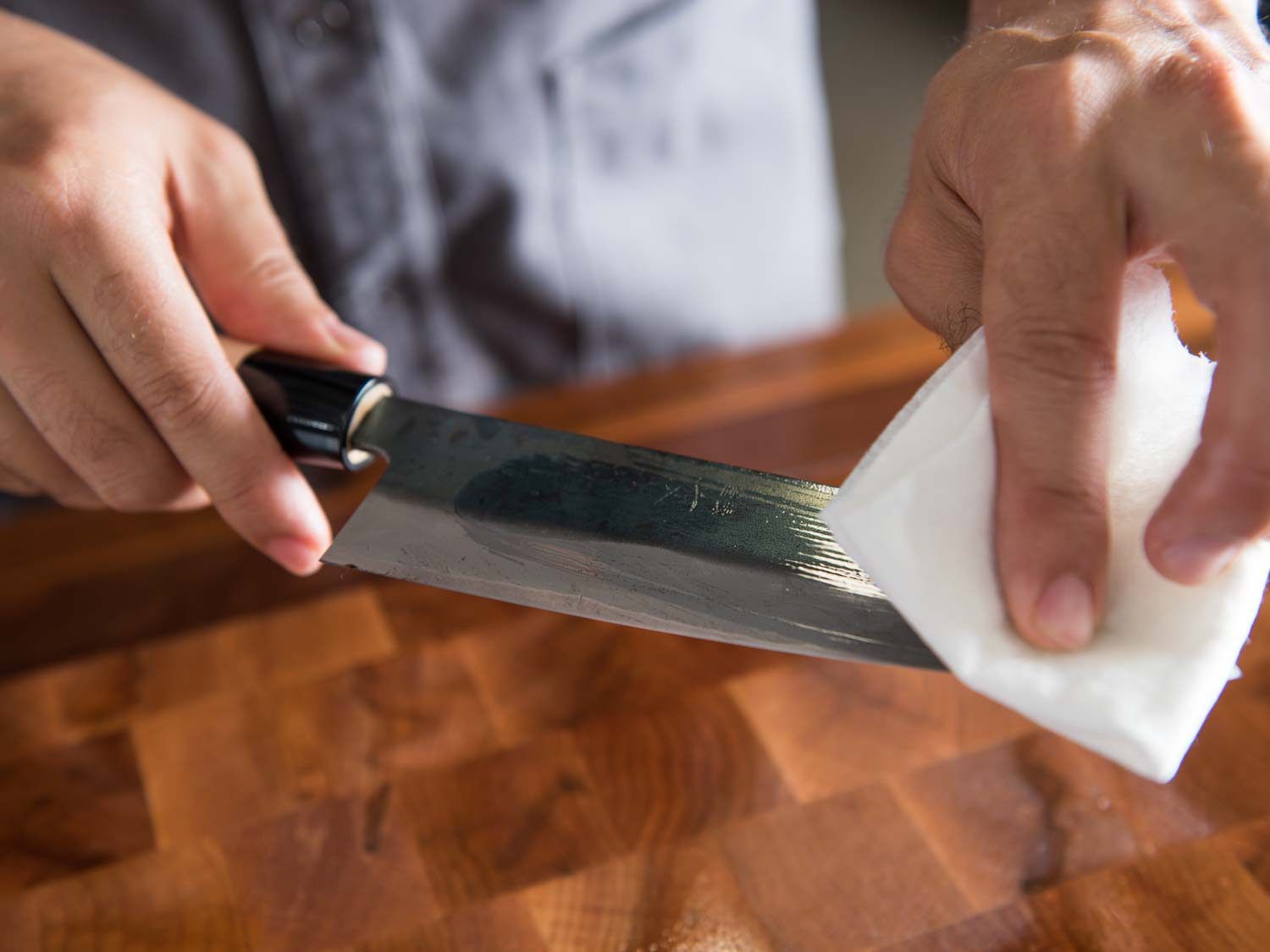 Hands using white cloth to wipe mineral oil over knife blade
