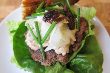 Closeup of a duck burger with pickled fennel and prune mayonnaise, ready to be assembled with the top half of a brioche bun.
