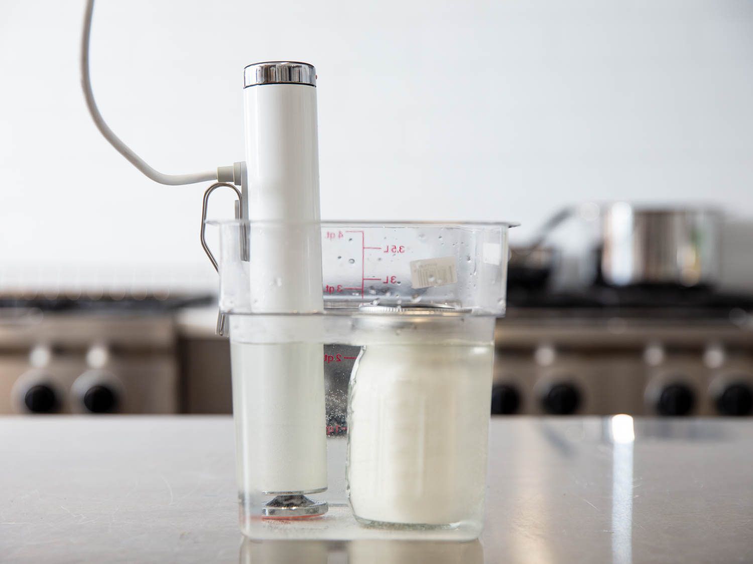 An immersion circulator is used to incubate homemade yogurt in a mason jar on a table.